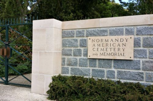 entrance gate to Normandy American Cemetery made of gray stone and a green iron gate