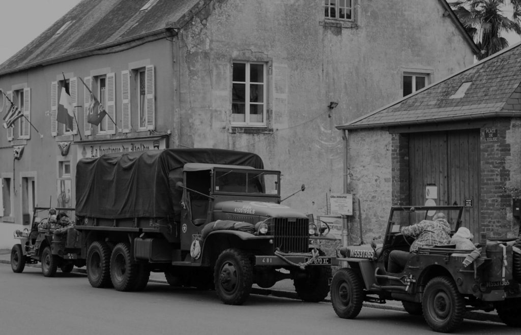 army truck and 2 jeeps from wwii on the street in a french village