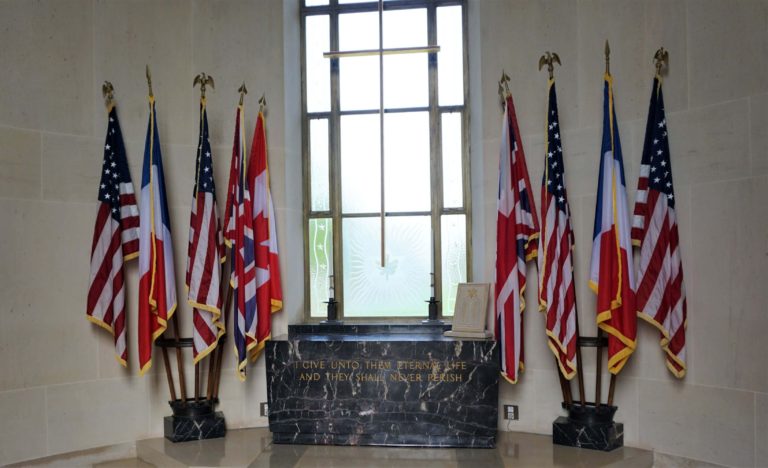 Normandy American Cemetery interior chapel with black marble alter with flags on the side and glass window with a cross