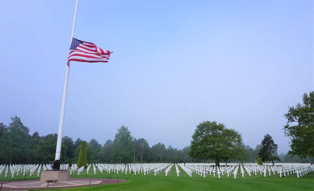 U.S flag flying at half staff with cross shaped grave markers at Normandy American Cemetery